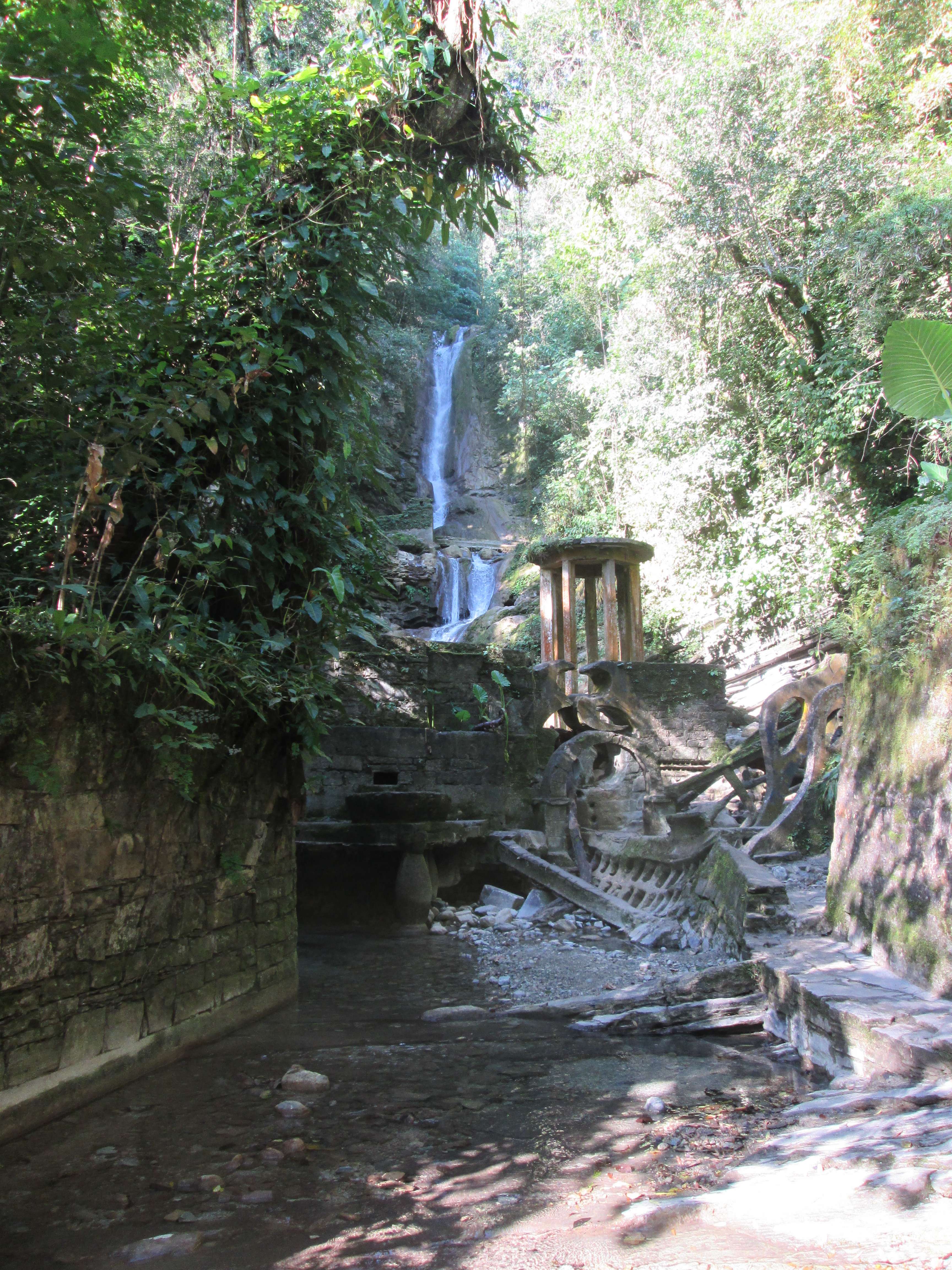 A path alongside a stream, with artificial concrete ruins and a waterfall in the background