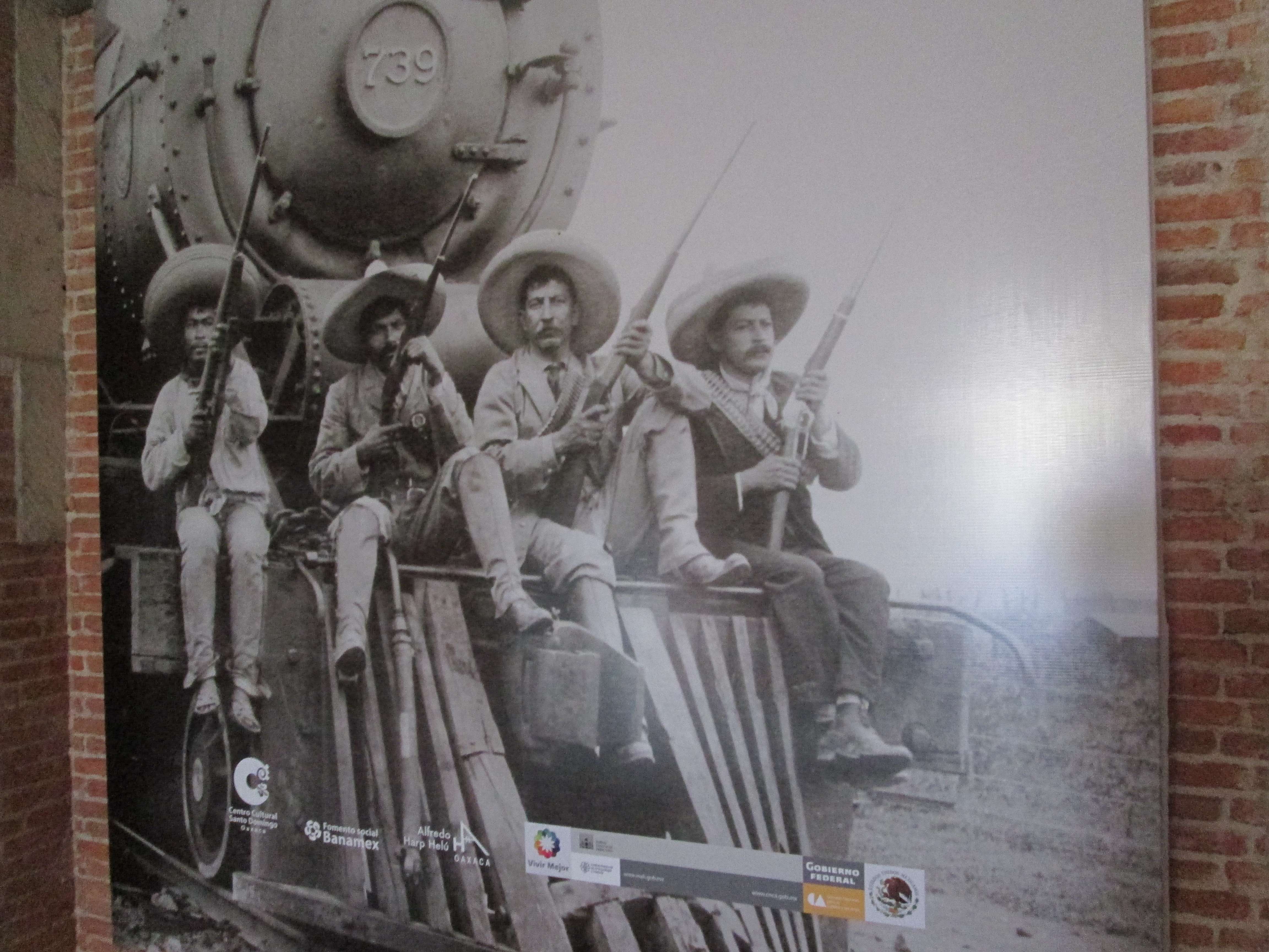 A photo of photo of four men sitting on the cow catcher of a train, holding rifles